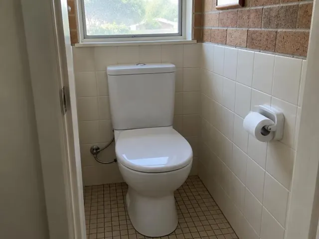 Clean white toilet in a small tiled bathroom with a window in St Ives