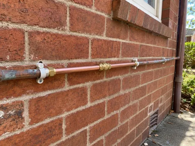 Repaired copper water pipe along a brick exterior wall near a window in Pymble